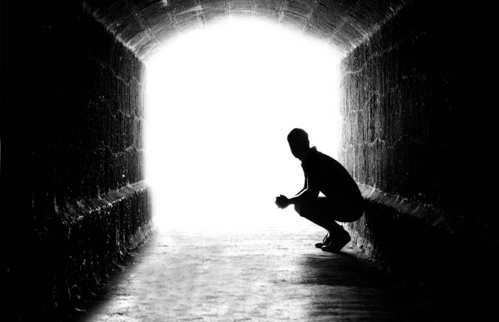 Human sitting silhouette in back-lit in tunnel exit